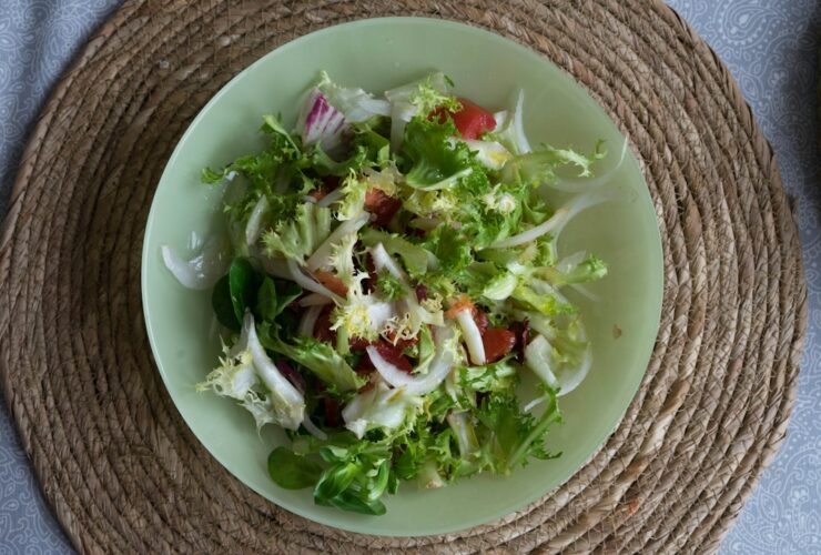 Overhead shot of Asian spiralized cucumber noodle salad in a wide bowl, garnished with sesame seeds, sliced scallions, shredded carrots, and a drizzle of sesame-ginger dressing on a light linen surface