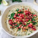 Baba Ganoush served in a shallow bowl drizzled with olive oil and topped with pomegranate seeds, fresh parsley, and a sprinkle of smoked paprika on a rustic wooden board
