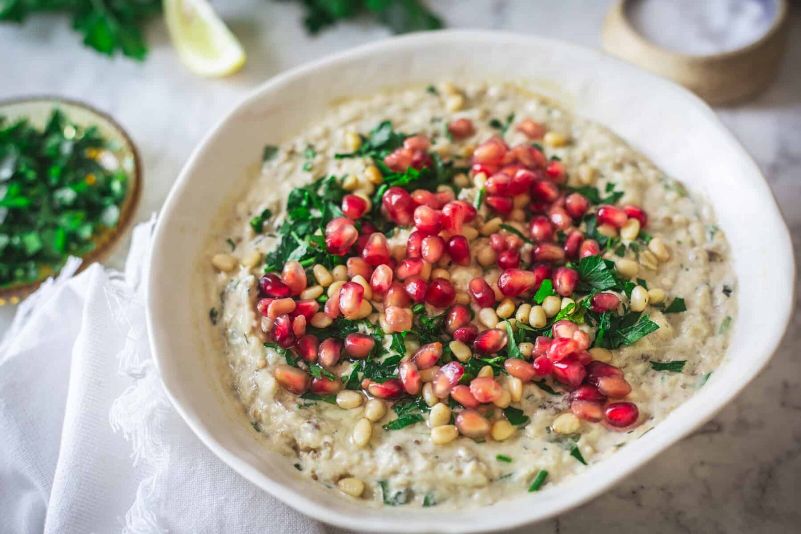 Baba Ganoush served in a shallow bowl drizzled with olive oil and topped with pomegranate seeds, fresh parsley, and a sprinkle of smoked paprika on a rustic wooden board