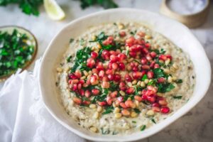 Baba Ganoush served in a shallow bowl drizzled with olive oil and topped with pomegranate seeds, fresh parsley, and a sprinkle of smoked paprika on a rustic wooden board