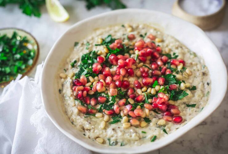 Baba Ganoush served in a shallow bowl drizzled with olive oil and topped with pomegranate seeds, fresh parsley, and a sprinkle of smoked paprika on a rustic wooden board