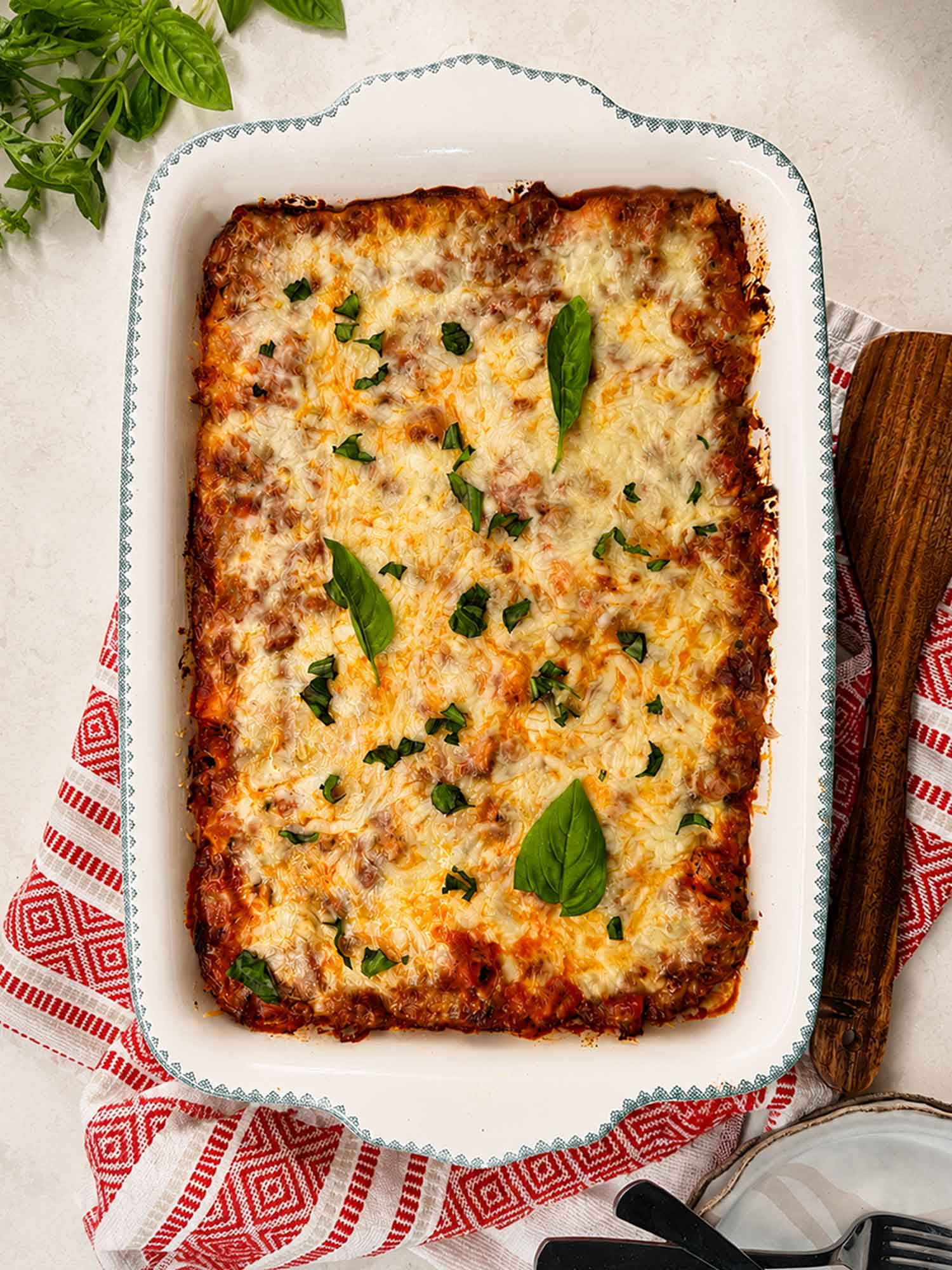 golden bubbly baked ziti in a white ceramic baking dish, fresh basil on top, rustic wooden table