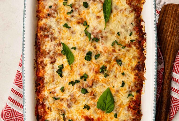 golden bubbly baked ziti in a white ceramic baking dish, fresh basil on top, rustic wooden table
