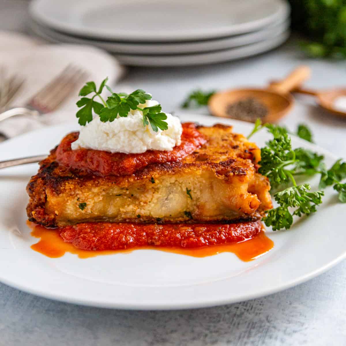 close-up of a serving of baked ziti being lifted from the pan showing layers of pasta, ricotta, and melted mozzarella with fresh basil garnish
