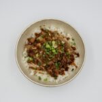 Beef and Broccoli Stir Fry served over steamed white rice in a white bowl, garnished with sesame seeds and sliced green onions, glossy garlic ginger sauce coating every piece