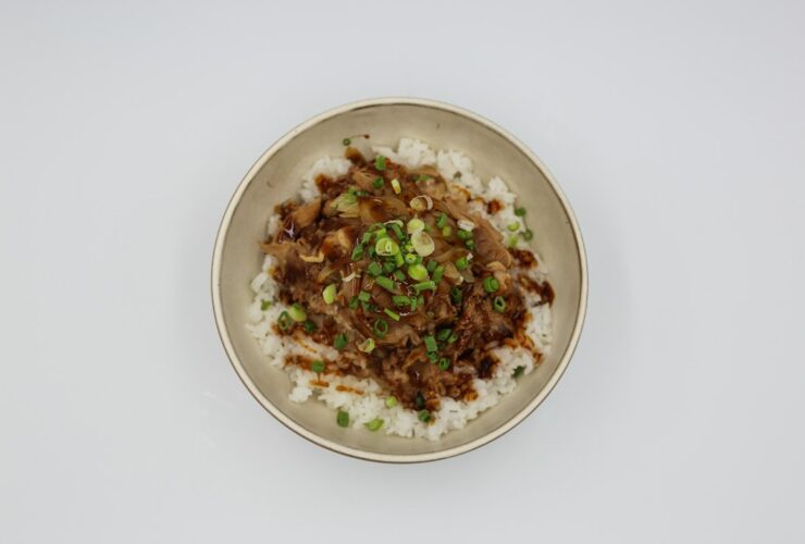 Beef and Broccoli Stir Fry served over steamed white rice in a white bowl, garnished with sesame seeds and sliced green onions, glossy garlic ginger sauce coating every piece