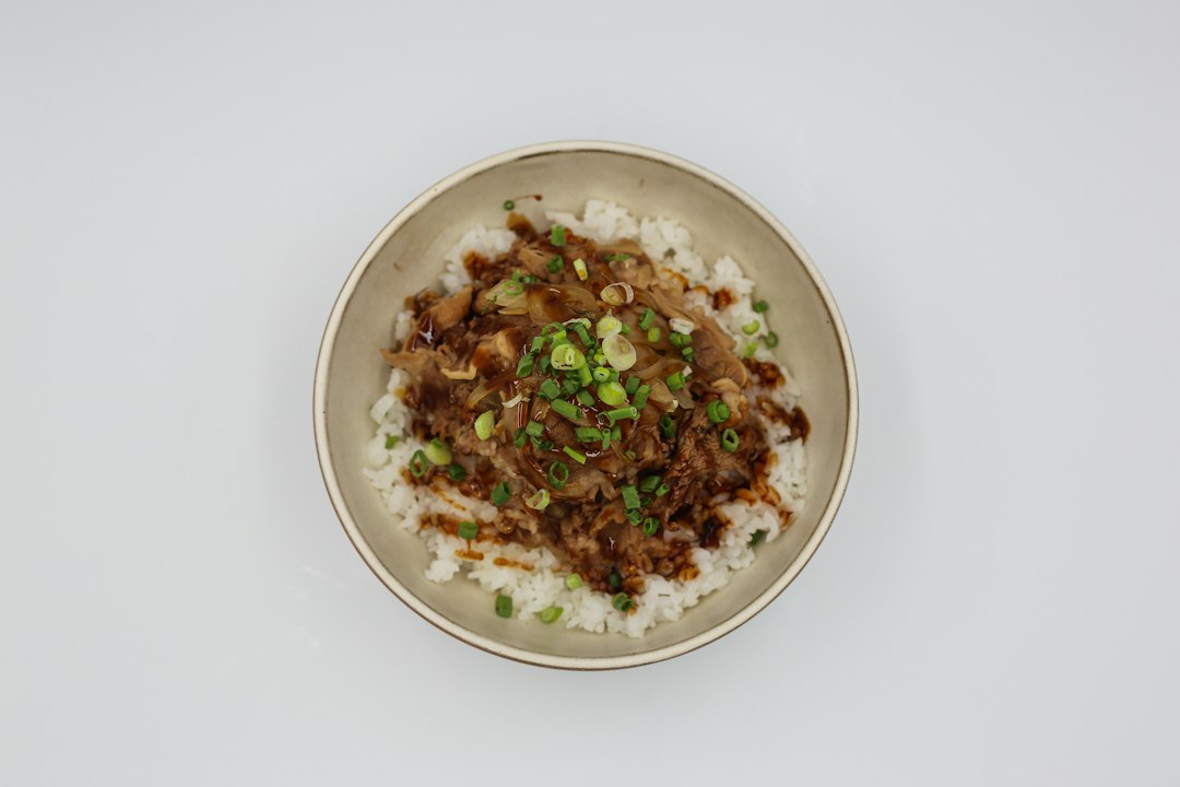 Beef and Broccoli Stir Fry served over steamed white rice in a white bowl, garnished with sesame seeds and sliced green onions, glossy garlic ginger sauce coating every piece