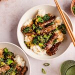 Beef and Broccoli Stir Fry served over steamed white rice in a white bowl, garnished with sesame seeds and sliced green onions, glossy garlic ginger sauce coating every piece