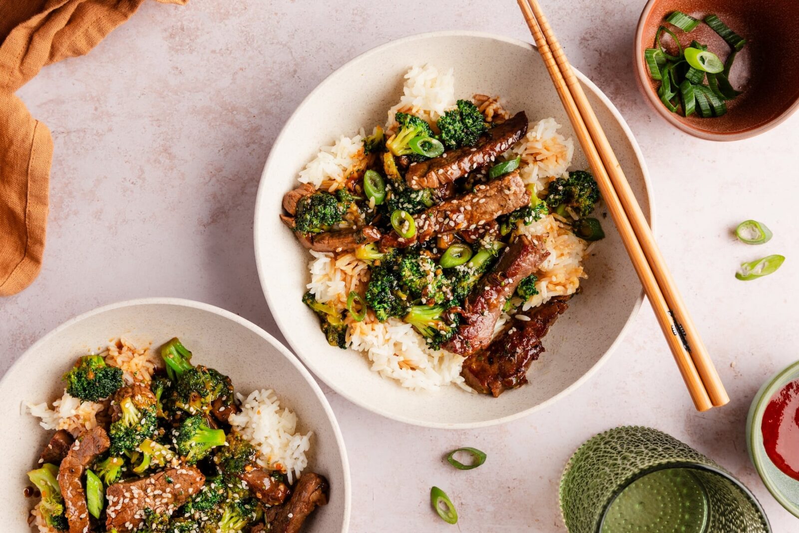 Beef and Broccoli Stir Fry served over steamed white rice in a white bowl, garnished with sesame seeds and sliced green onions, glossy garlic ginger sauce coating every piece