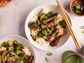 Beef and Broccoli Stir Fry — Better-Than-Takeout with Glossy Garlic Ginger Sauce 20 Beef and Broccoli Stir Fry served over steamed white rice in a white bowl, garnished with sesame seeds and sliced green onions, glossy garlic ginger sauce coating every piece