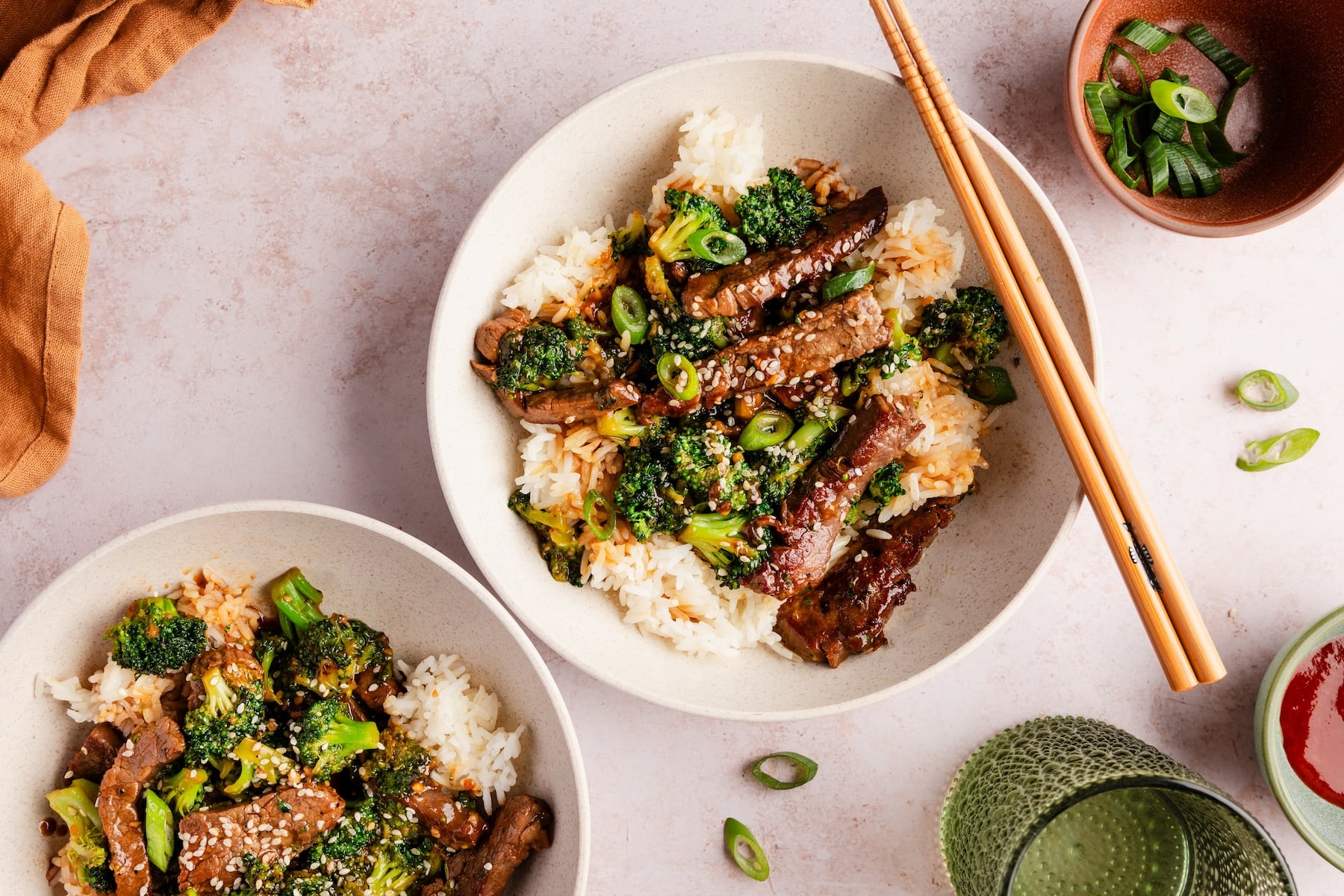 Beef and Broccoli Stir Fry served over steamed white rice in a white bowl, garnished with sesame seeds and sliced green onions, glossy garlic ginger sauce coating every piece