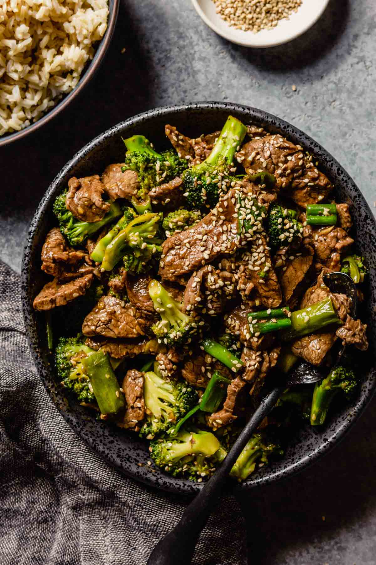 Overhead flat-lay of stir fry ingredients prepped and arranged — sliced flank steak, broccoli florets, minced garlic, grated ginger, soy sauce, oyster sauce, and cornstarch in small bowls ready to cook
