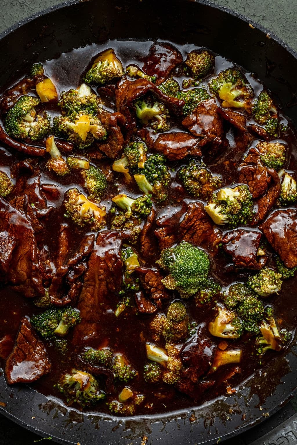 Close-up of Beef and Broccoli Stir Fry in a wok with glossy garlic ginger sauce coating tender beef strips and vibrant green broccoli florets, sesame seeds scattered on top