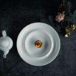 Bisque Cheesecake sliced and beautifully plated on a white ceramic plate with a smooth, creamy filling and golden graham cracker crust, garnished with a light dusting of spice and fresh herbs