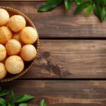 Golden Brazilian Pão de Queijo cheese puffs piled in a rustic linen-lined basket on a wooden board, beautifully lit with a warm overhead angle
