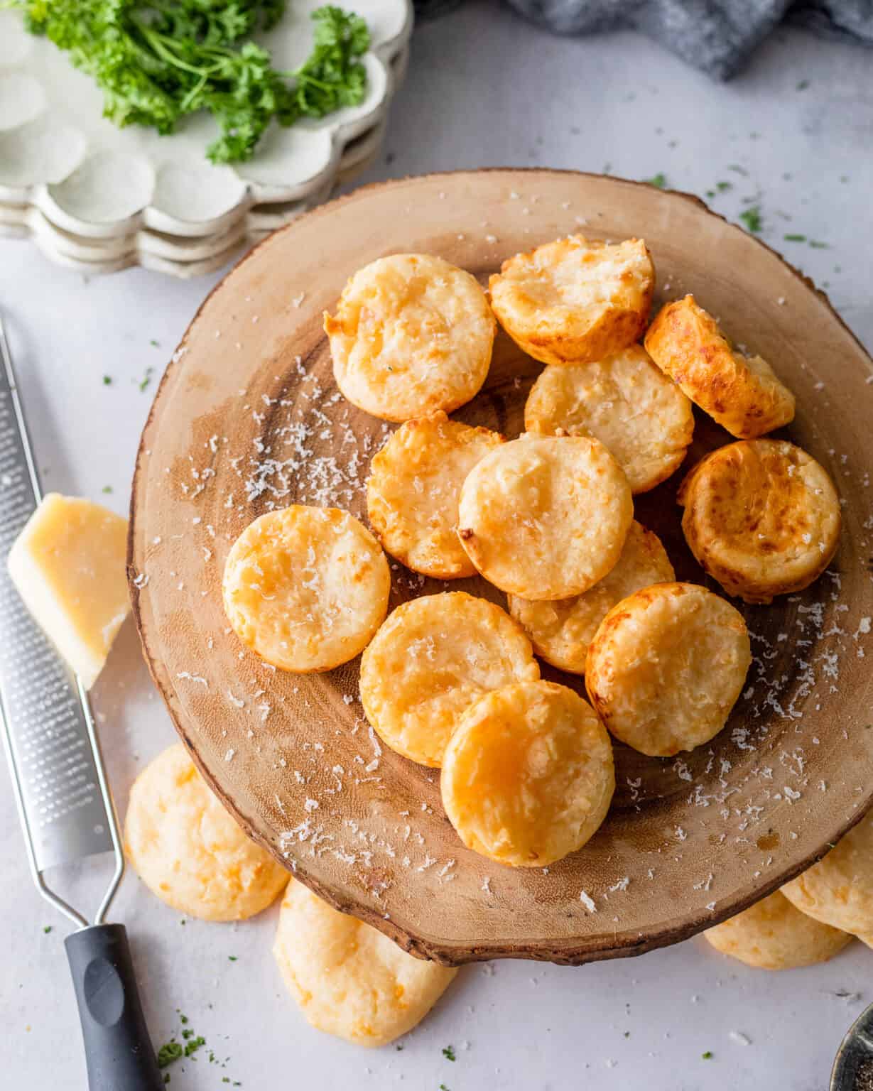 Close-up of a split-open Brazilian Pão de Queijo cheese puff showing the airy, chewy, golden interior with melted cheese strands, served on a wooden board with a cup of coffee in the background