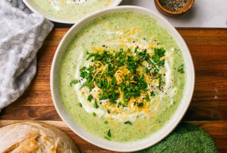 Broccoli Cheddar Soup — Velvety, From-Scratch Comfort That Beats the Café 27 A rustic bowl of broccoli cheddar soup garnished with shredded cheddar and broccoli florets, photographed on a wooden table with warm natural light
