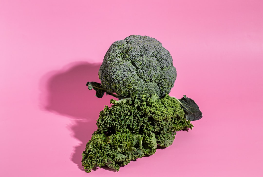 Overhead flat-lay of broccoli cheddar soup ingredients — fresh broccoli, block of sharp cheddar, onion, garlic, butter, cream, and spices arranged on a white marble surface