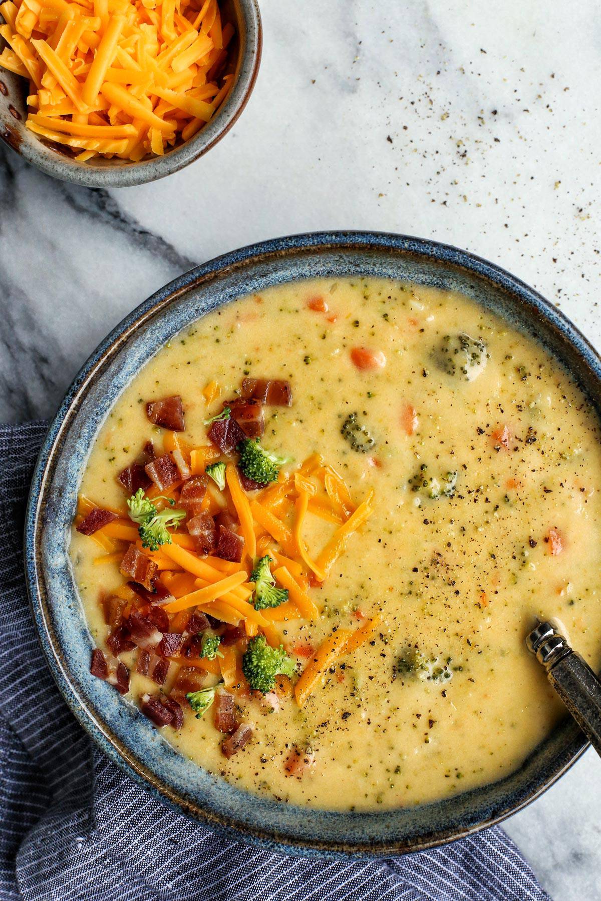 Close-up of a ladle lifting velvety broccoli cheddar soup from a pot, showing the rich golden color and visible broccoli pieces, with steam rising