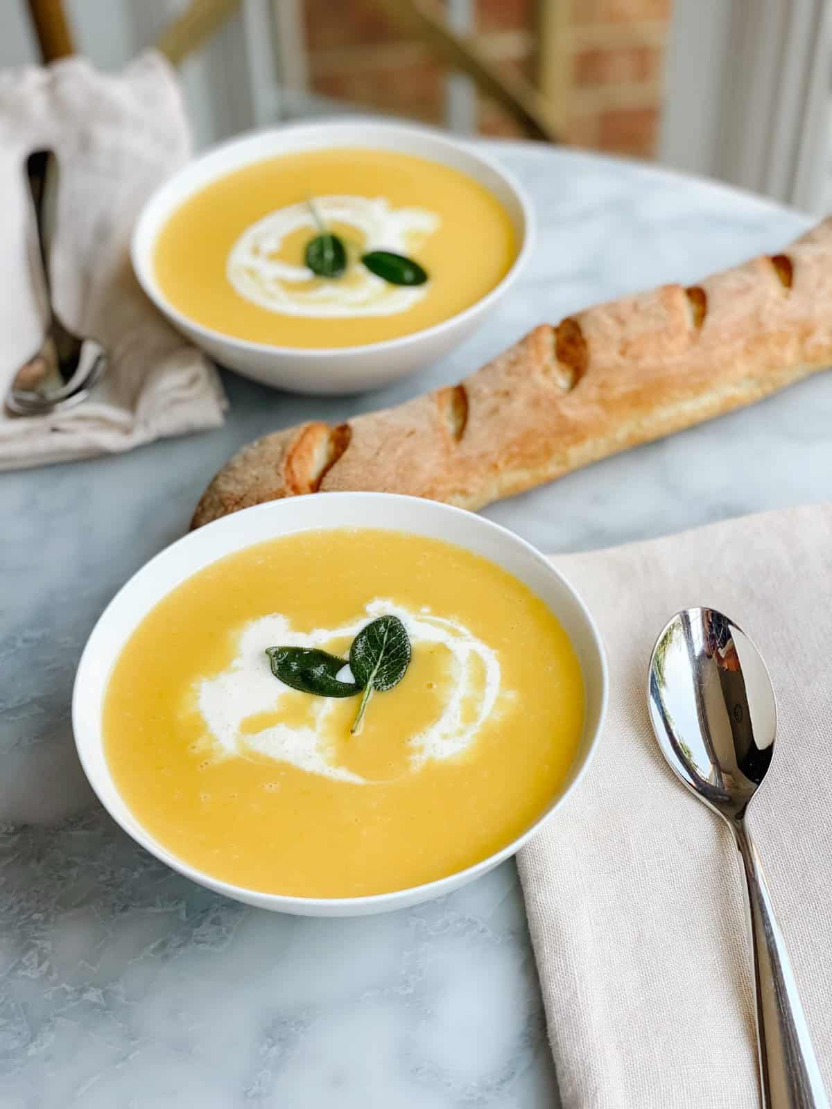 Butternut Squash Soup — Silky Roasted Squash Soup with Sage and Cream 26 Silky butternut squash soup in a white bowl topped with a swirl of cream, crispy sage leaves, and cracked black pepper, photographed overhead on a rustic wooden table with autumn leaves