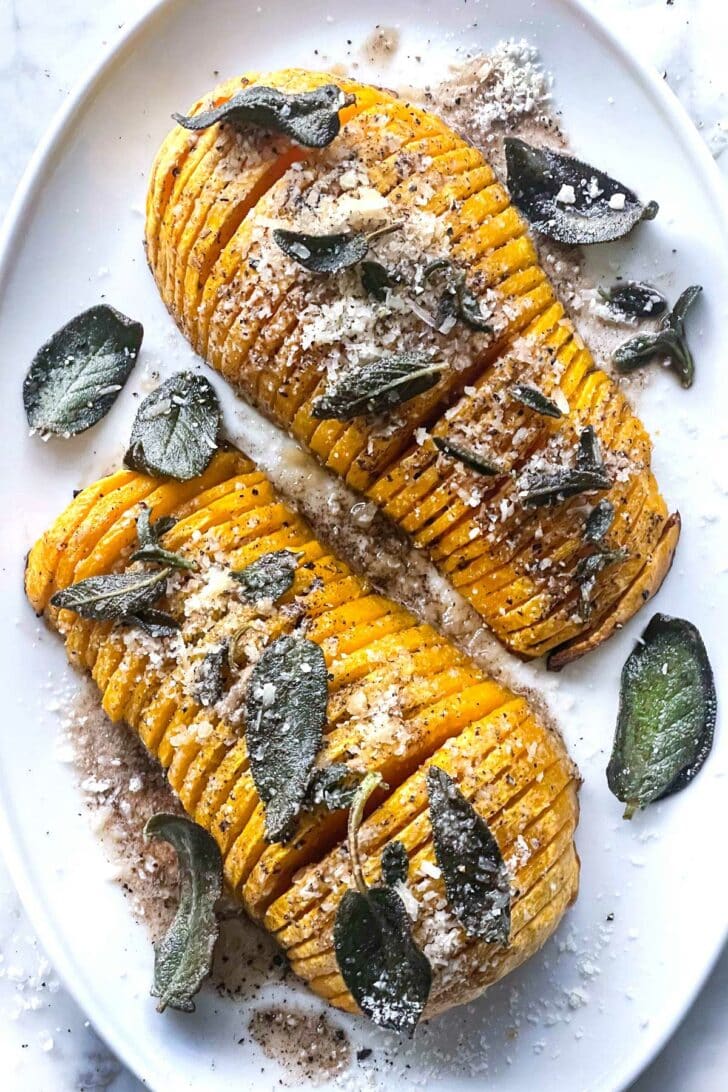 Butternut Squash Soup — Silky Roasted Squash Soup with Sage and Cream 27 Halved butternut squash cut-side-up on a baking sheet drizzled with olive oil, garlic cloves nearby, sage leaves scattered around, ready for roasting