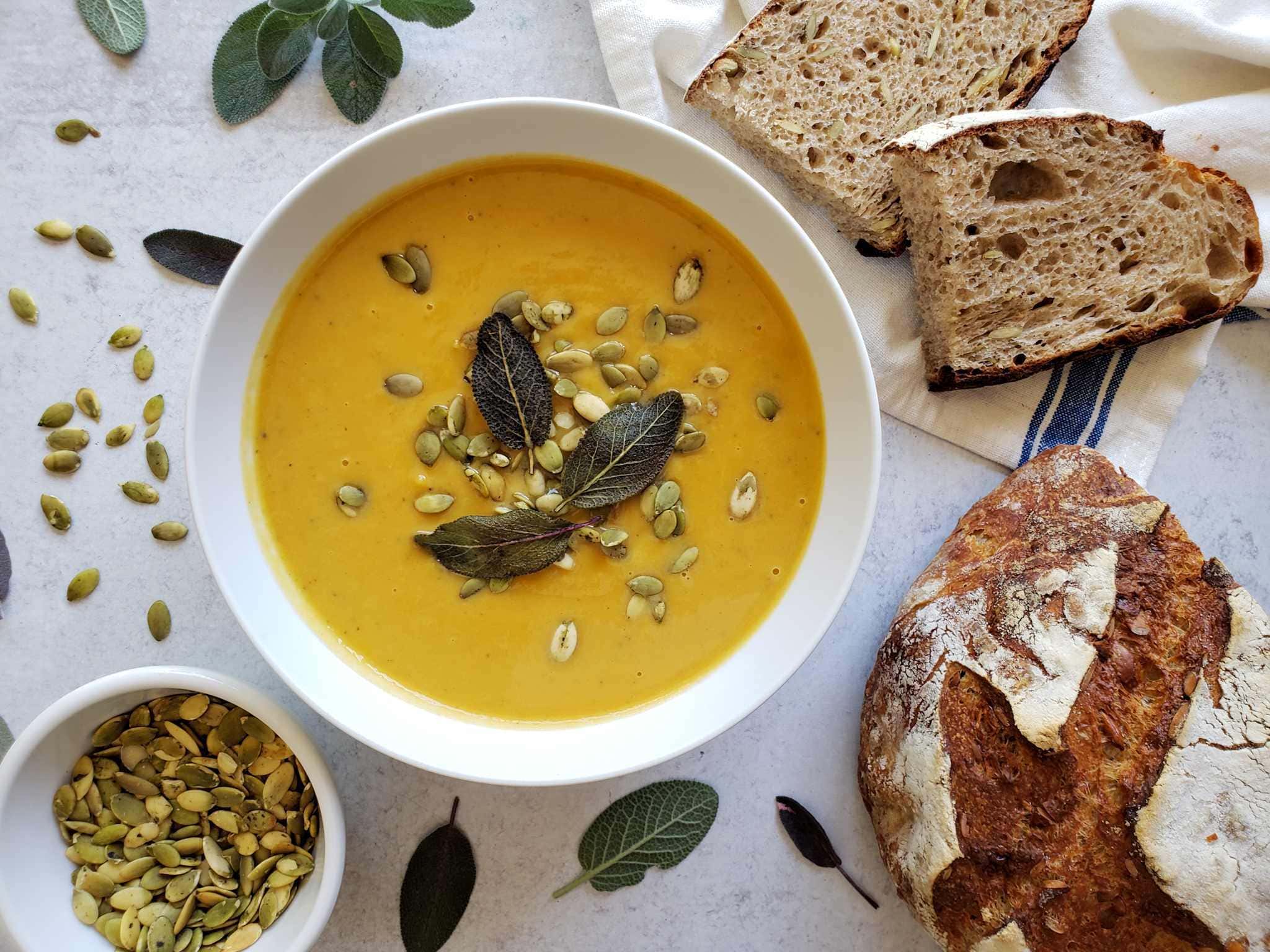Butternut Squash Soup — Silky Roasted Squash Soup with Sage and Cream 28 Close-up of butternut squash soup in a ceramic bowl with a swirl of cream, a few crispy fried sage leaves, toasted pepitas, and a drizzle of olive oil, warm autumn tones