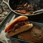 Campfire Sloppy Joes served on toasted brioche buns beside a glowing campfire, garnished with pickles and coleslaw