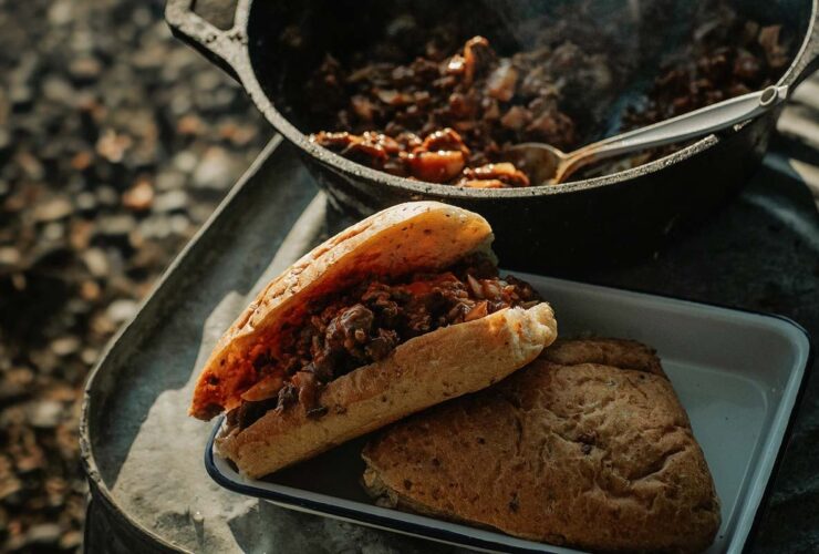 Campfire Sloppy Joes served on toasted brioche buns beside a glowing campfire, garnished with pickles and coleslaw
