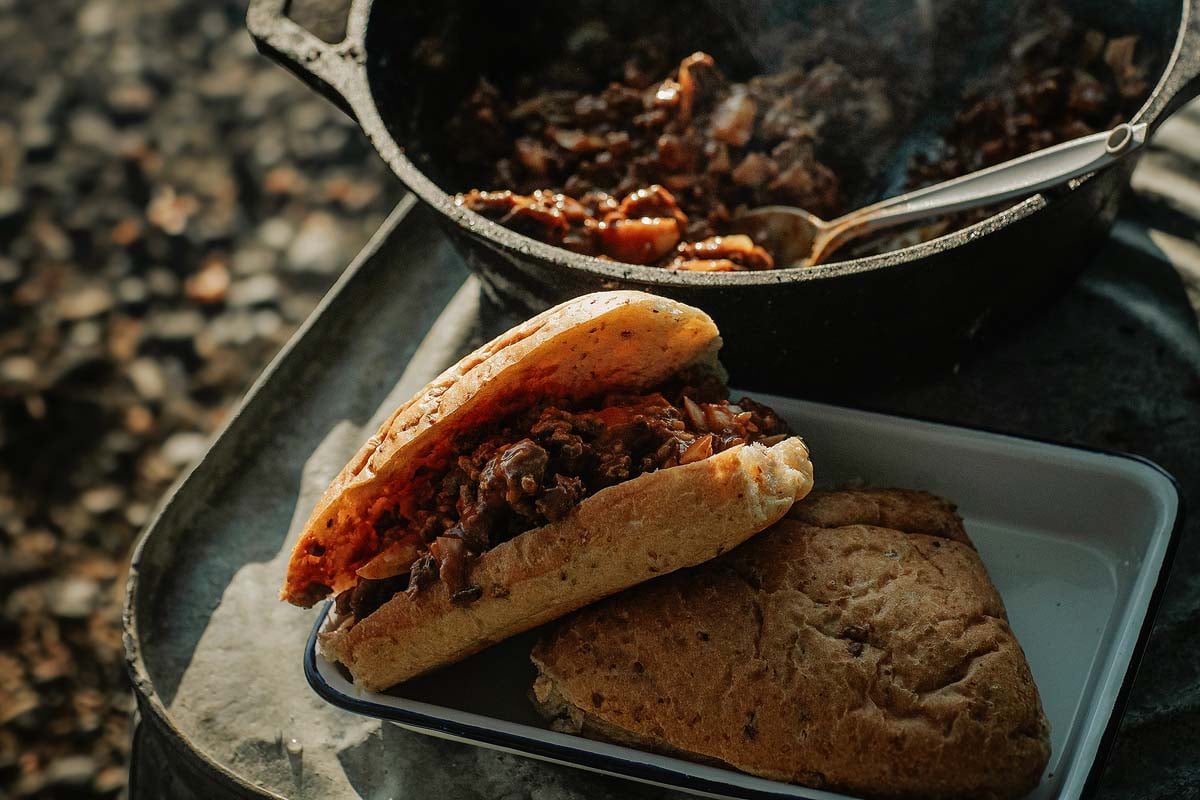 Campfire Sloppy Joes — Tangy, Make-Ahead Ground Beef for the Crowd 27 Cast iron skillet with tangy ground beef Sloppy Joe filling simmering over a campfire grate, surrounded by camping cookware and fresh bun ingredients