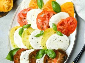 Beautiful Caprese Salad arranged on a white platter with sliced heirloom tomatoes, fresh mozzarella, basil leaves, and a drizzle of balsamic glaze and olive oil