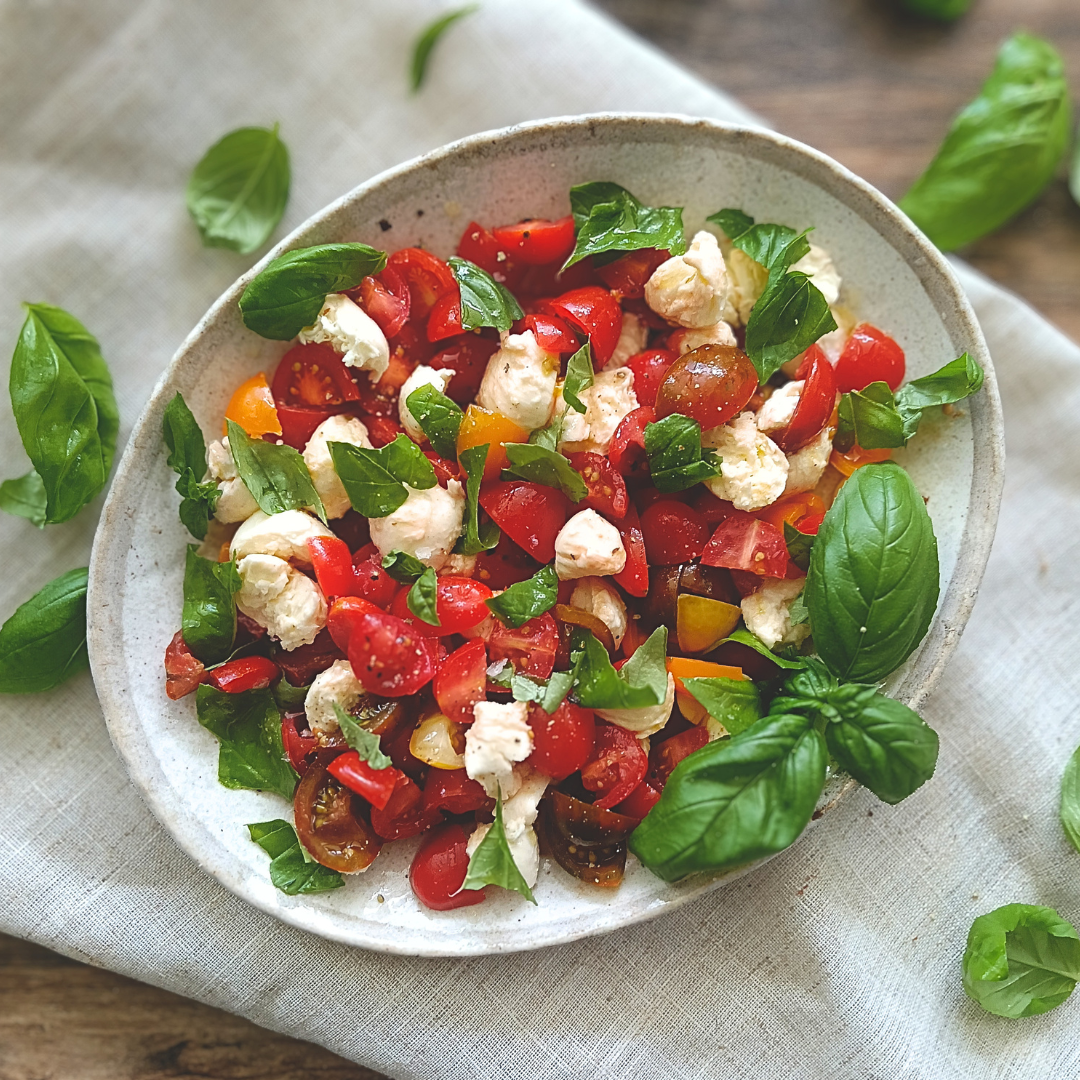 Close-up of a single serving of Caprese Salad showing the layers of tomato, mozzarella, and basil with a glossy balsamic glaze drizzle and flaky sea salt crystals