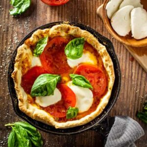 Cast Iron Skillet Pizza — The Ultimate Campground Pizza Night Recipe 13 Cast iron skillet pizza with golden crispy crust, bubbling mozzarella cheese, and fresh basil leaves, photographed outdoors near a campfire