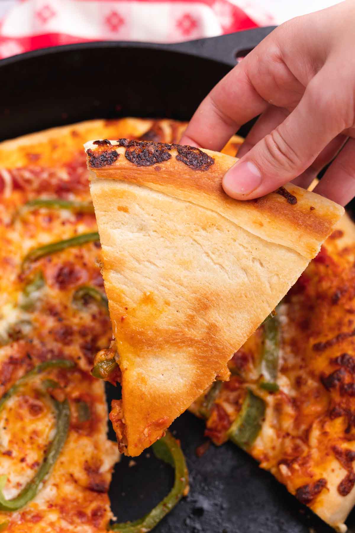 Close-up of a cast iron skillet pizza slice being lifted to show the crispy golden bottom crust and stretchy melted mozzarella cheese