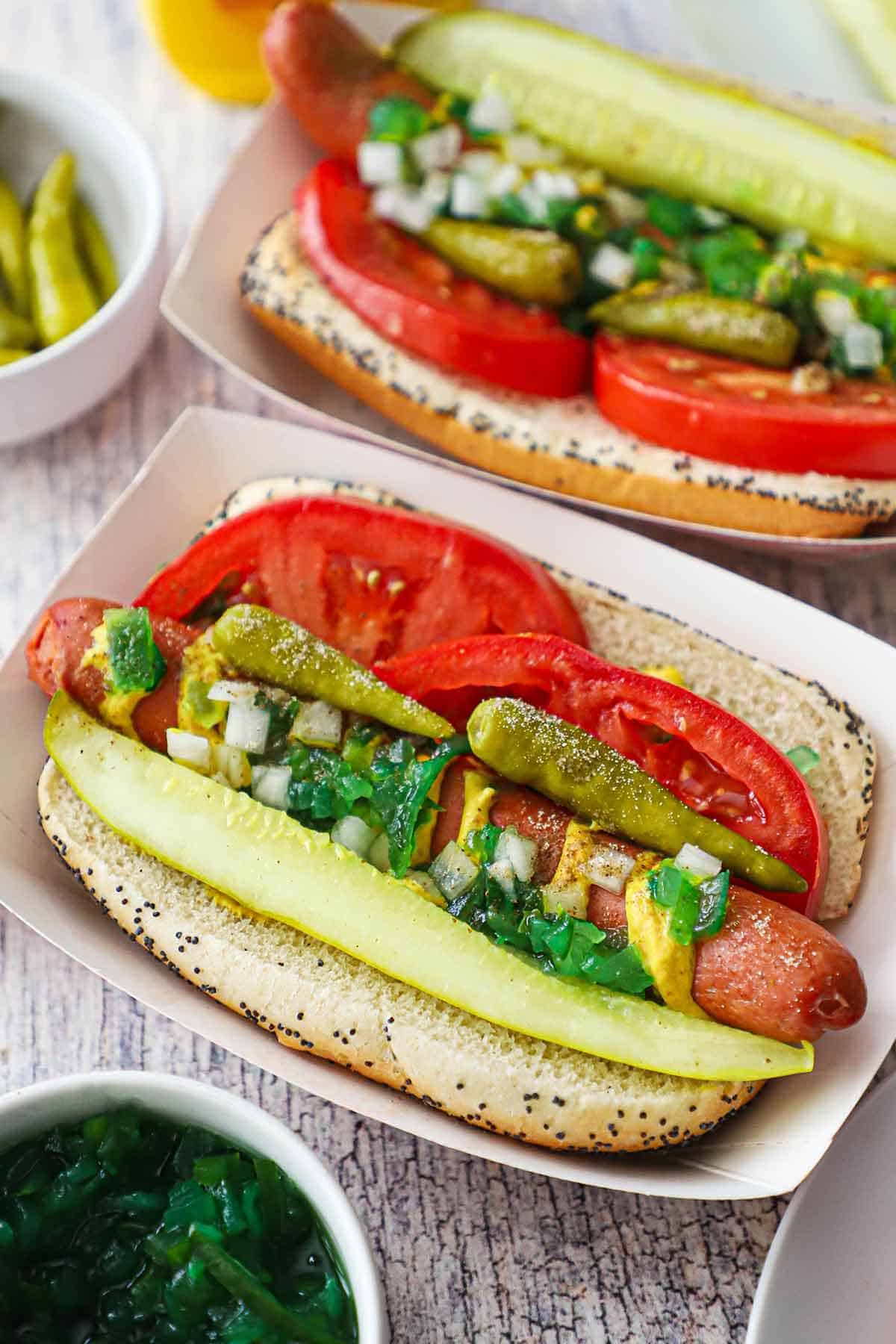 Chicago Style Hot Dogs — The Dragged Through the Garden Classic Done Right 27 Chicago style hot dog ingredients laid out flat on white marble surface — tomatoes, pickle spears, sport peppers, relish, mustard, celery salt, poppy seed buns, and all-beef frankfurters