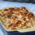 Chicken Bacon Ranch Pasta Bake served in a white baking dish, golden and bubbling with melted cheddar, fresh chives on top, rustic wooden table background