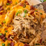 Chicken Bacon Ranch Pasta Bake served in a white baking dish, golden and bubbling with melted cheddar, fresh chives on top, rustic wooden table background