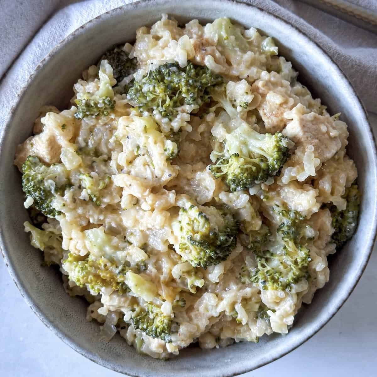 Overhead flat lay of casserole ingredients — shredded rotisserie chicken, raw broccoli florets, uncooked rice, shredded cheddar, cream of mushroom soup, and chicken broth on a white marble surface