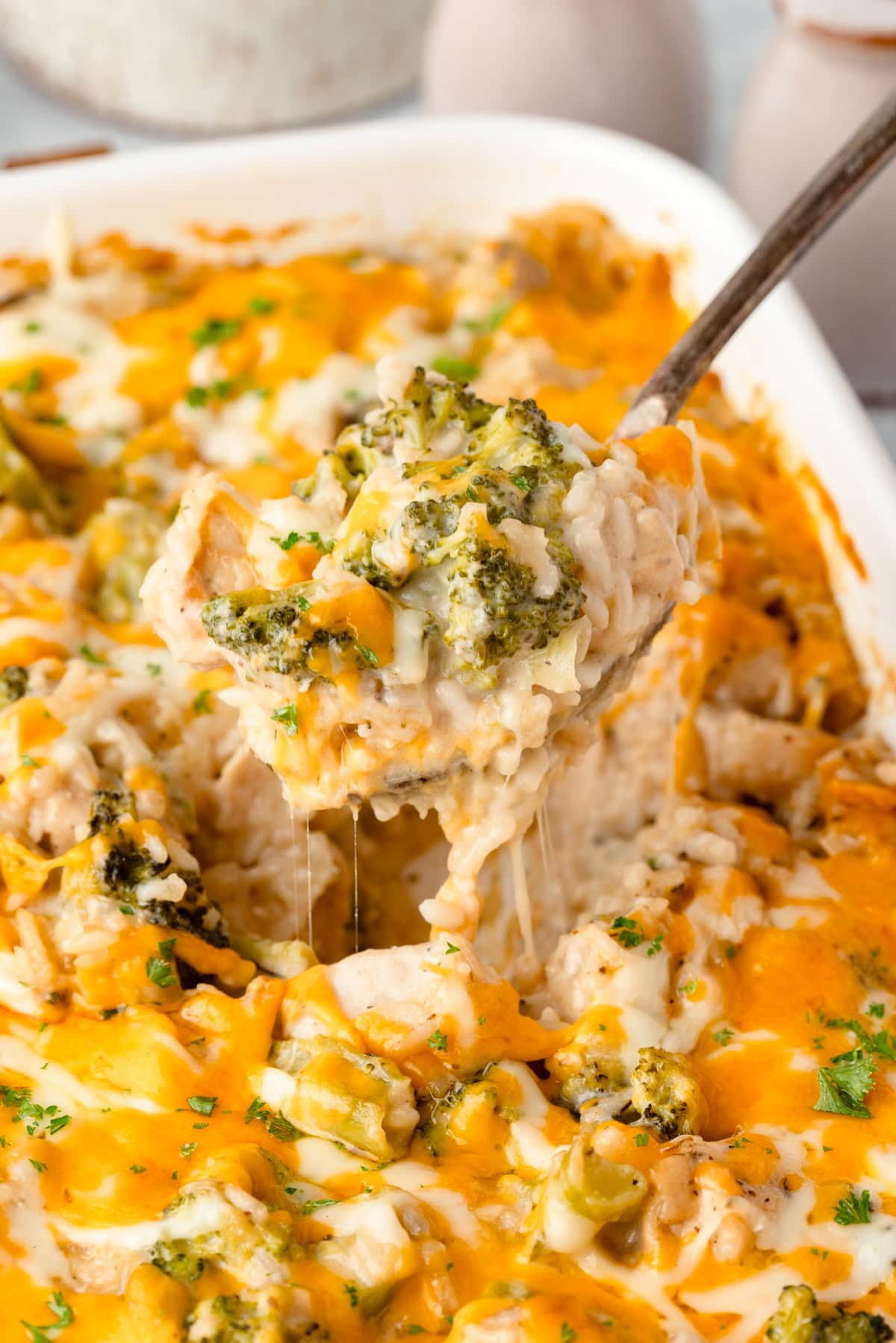 Close-up of a serving of chicken broccoli rice casserole on a white plate, steam rising, showing creamy rice, green broccoli, and golden melted cheese