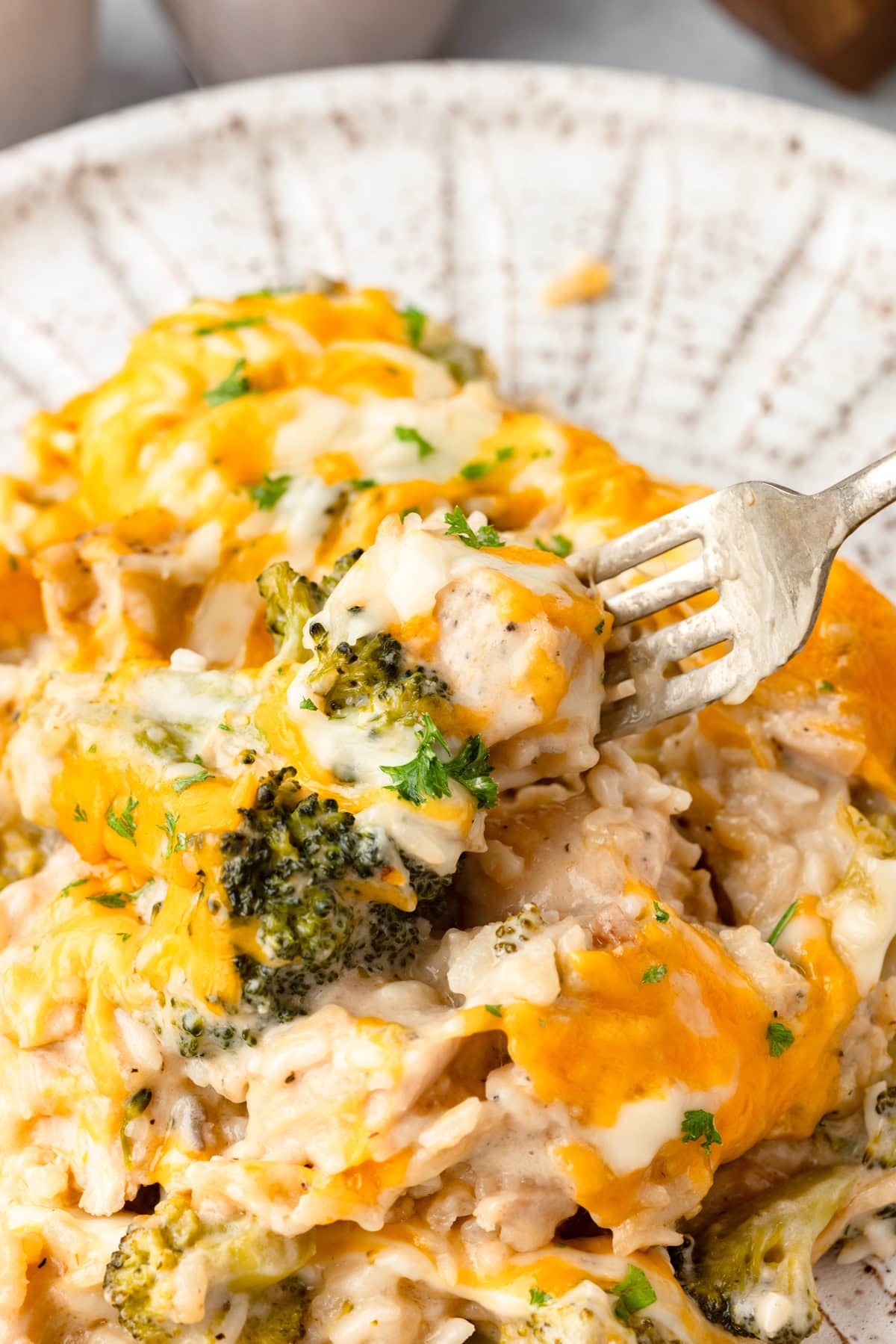 close-up of a serving of chicken broccoli rice casserole on a white plate showing the creamy interior with tender broccoli and shredded chicken topped with melted golden cheddar cheese