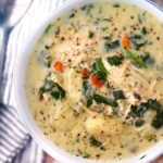 A rustic white bowl filled with creamy chicken gnocchi soup, pillowy gnocchi, shredded carrots, and spinach, garnished with cracked black pepper and fresh thyme, photographed from above on a warm linen surface