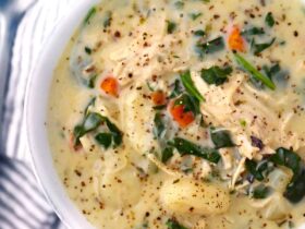 A rustic white bowl filled with creamy chicken gnocchi soup, pillowy gnocchi, shredded carrots, and spinach, garnished with cracked black pepper and fresh thyme, photographed from above on a warm linen surface