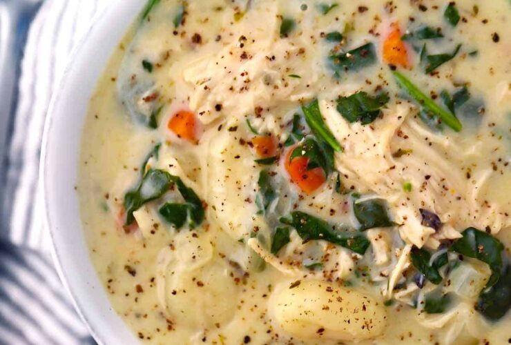 A rustic white bowl filled with creamy chicken gnocchi soup, pillowy gnocchi, shredded carrots, and spinach, garnished with cracked black pepper and fresh thyme, photographed from above on a warm linen surface