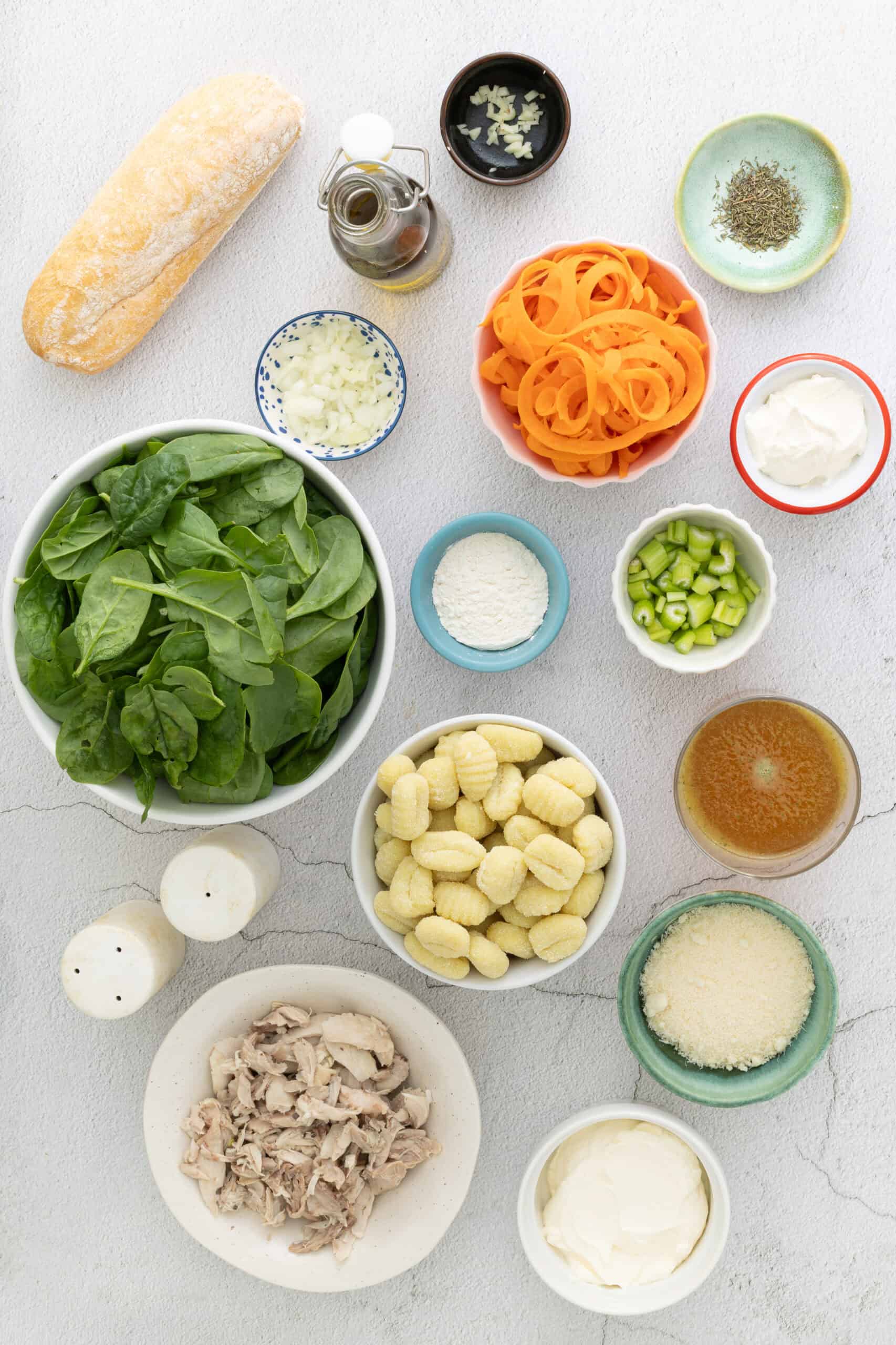 Overhead flat lay of chicken gnocchi soup ingredients arranged on a marble surface — raw chicken breast, shelf-stable gnocchi package, shredded carrots, baby spinach, half-and-half, chicken broth, garlic, onion, celery, and fresh thyme