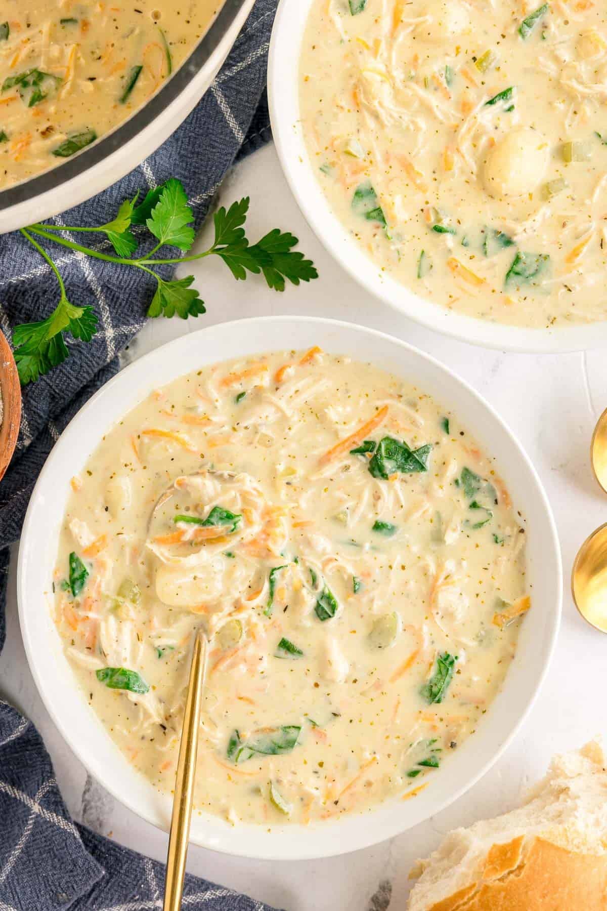 A close-up shot of a spoonful of chicken gnocchi soup being lifted from a bowl, showing pillowy gnocchi, shredded carrot, and creamy broth, with a warm blurred background