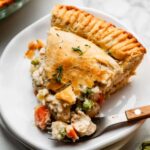 golden homemade chicken pot pie with flaky double crust, sliced open to reveal creamy vegetable filling, styled on a rustic wooden table