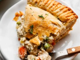 golden homemade chicken pot pie with flaky double crust, sliced open to reveal creamy vegetable filling, styled on a rustic wooden table