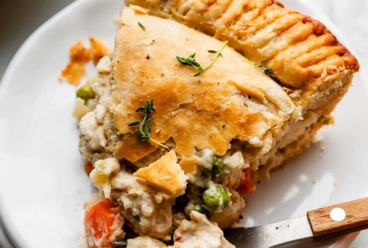 golden homemade chicken pot pie with flaky double crust, sliced open to reveal creamy vegetable filling, styled on a rustic wooden table