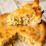 golden chicken pot pie with flaky crust fresh from the oven, steam rising, beautifully plated on a rustic wooden table