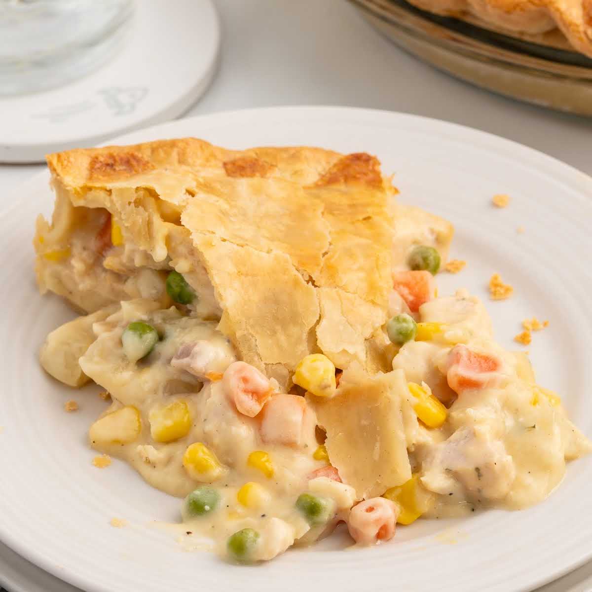 Chicken Pot Pie — Creamy Filling, Flaky Double Crust, Pure Comfort 28 close-up of a slice of chicken pot pie on a white plate, showing the layers of flaky golden crust and creamy vegetable-chicken filling, garnished with fresh thyme
