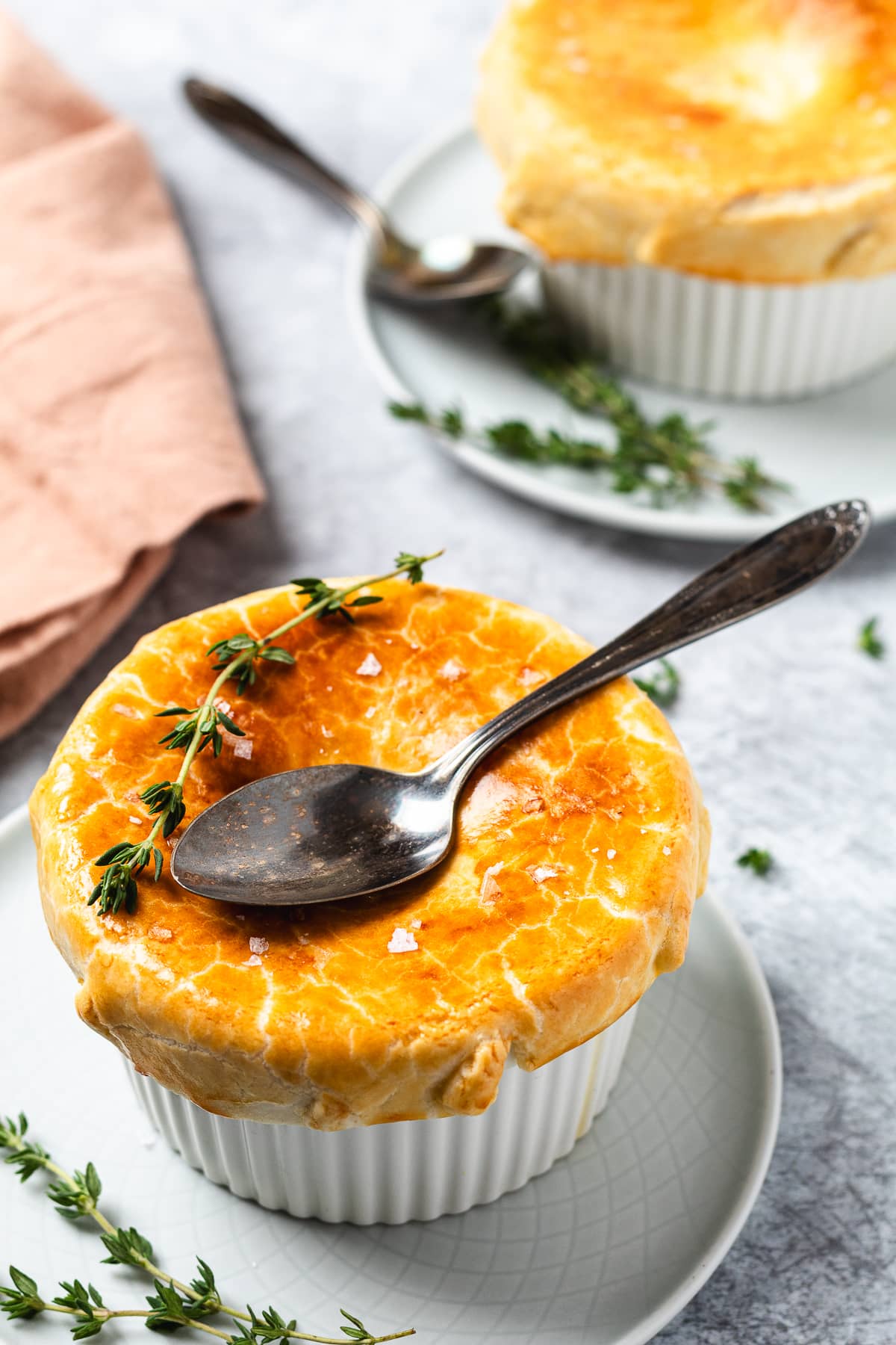 close-up of a slice of chicken pot pie being served, showing the creamy vegetable and chicken filling beneath a golden flaky crust, garnished with fresh thyme